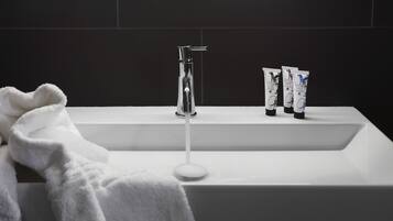 A white bathroom sink with a modern faucet, three toiletry bottles, and a white towel.