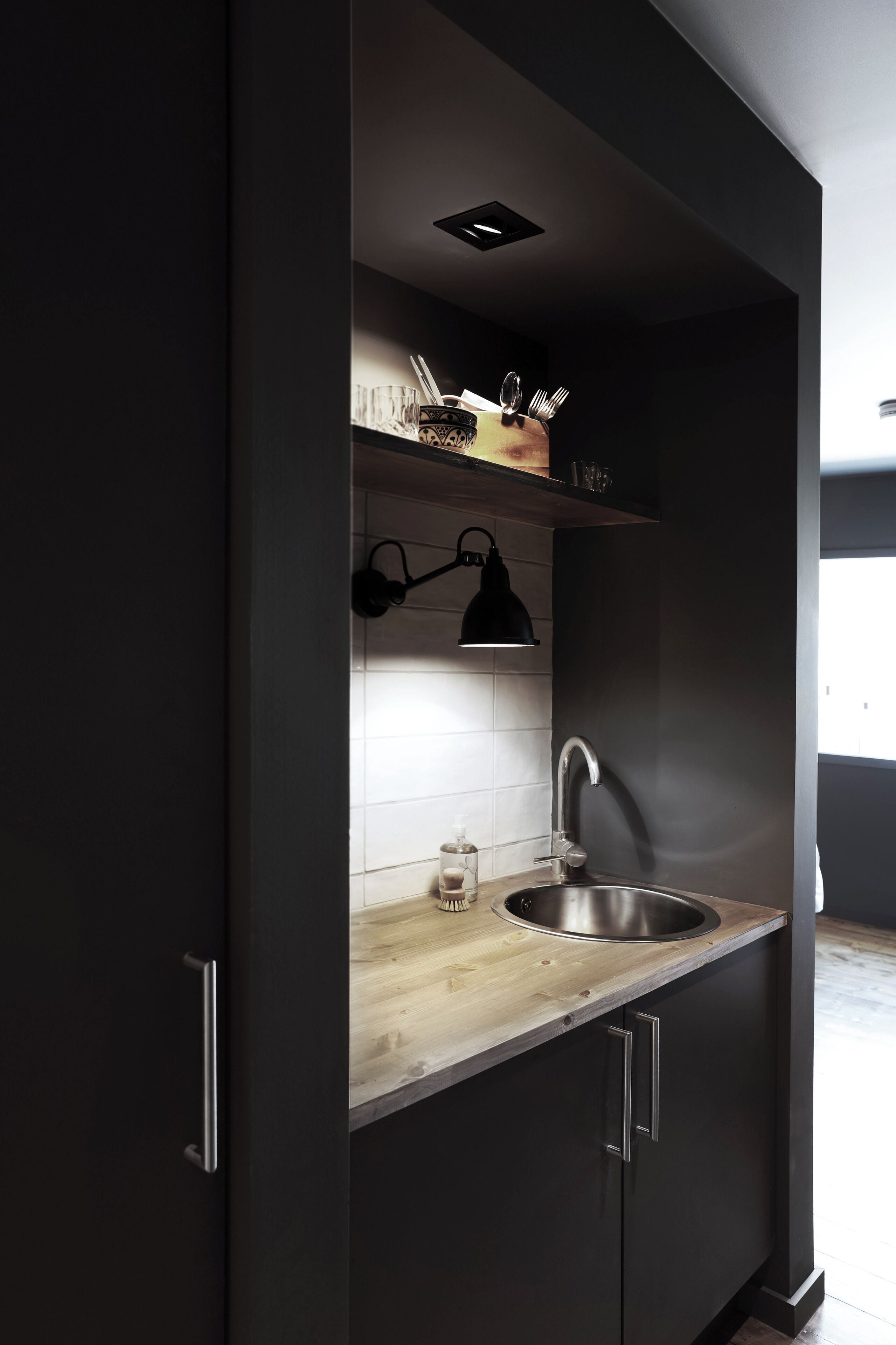 Una cocina moderna con armarios oscuros, encimera de madera, pileta de acero inoxidable y una lámpara colgante.