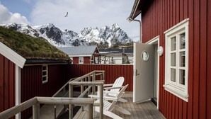 Un bâtiment rouge avec une terrasse en bois, une porte blanche et une vue sur des montagnes enneigées.