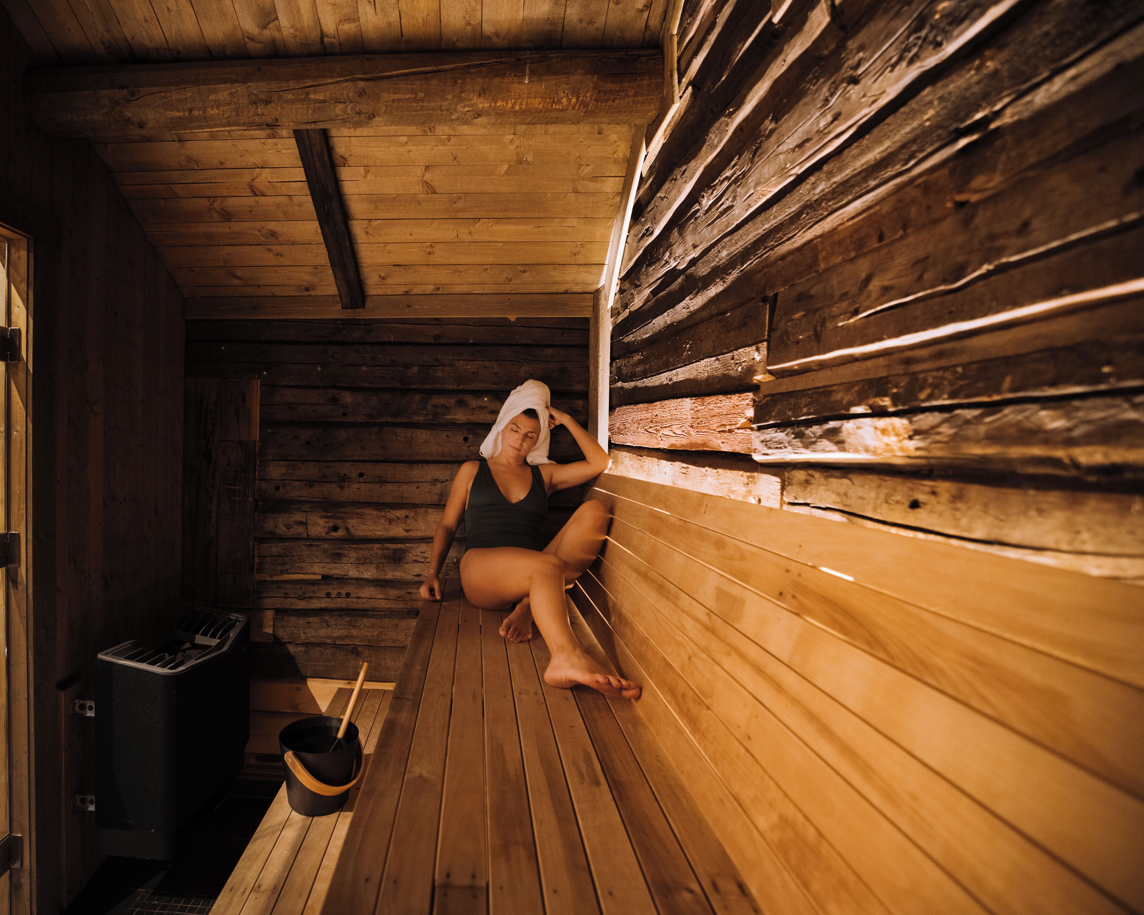 A sauna with wooden walls and benches, a bucket, and a wooden bench.