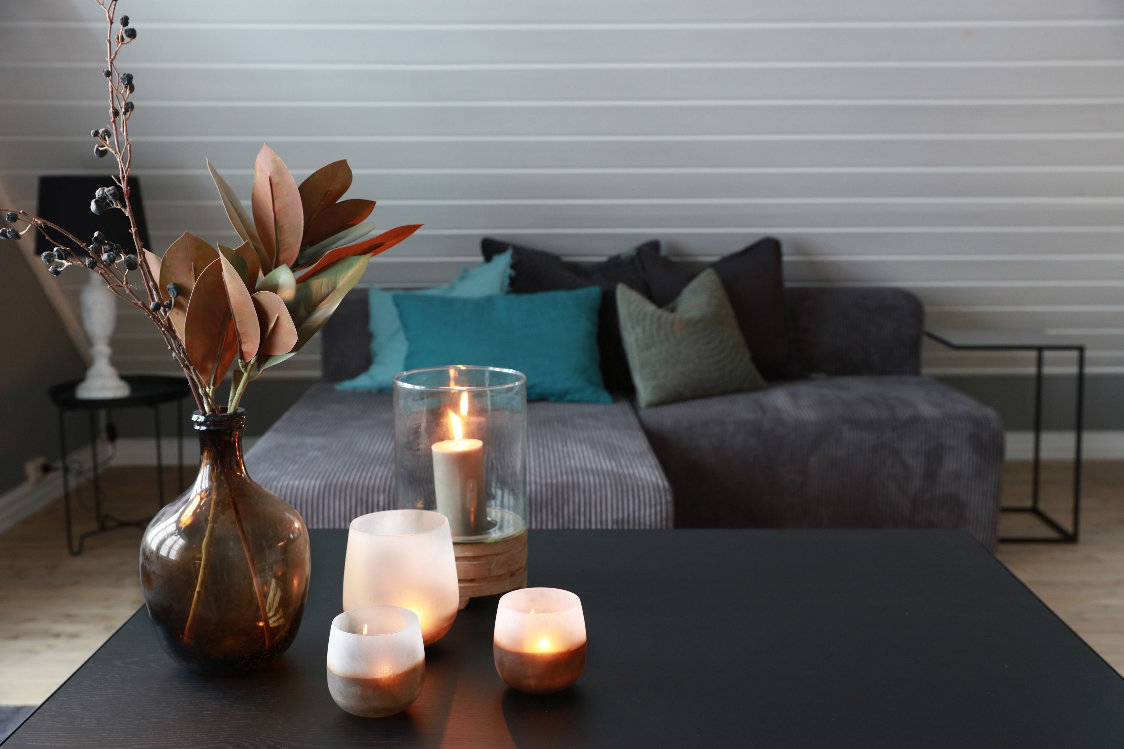 Una sala de estar moderna con una mesa de centro oscura, un jarrón con ramas secas y velas encendidas.