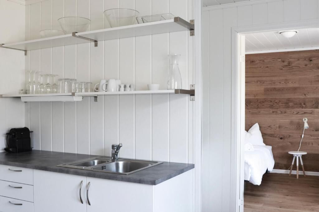 A modern kitchen with white cabinetry, a stainless steel sink, and open shelving with glassware.