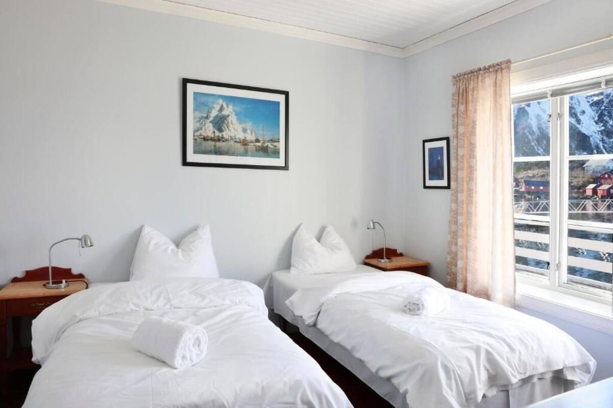 Une chambre d’hôtel avec deux lits simples, une fenêtre donnant sur un paysage enneigé et un tableau encadré au mur.