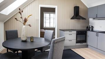 A modern kitchen with grey cabinetry, a black range hood, and a dining area with a round table and grey upholstered chairs.