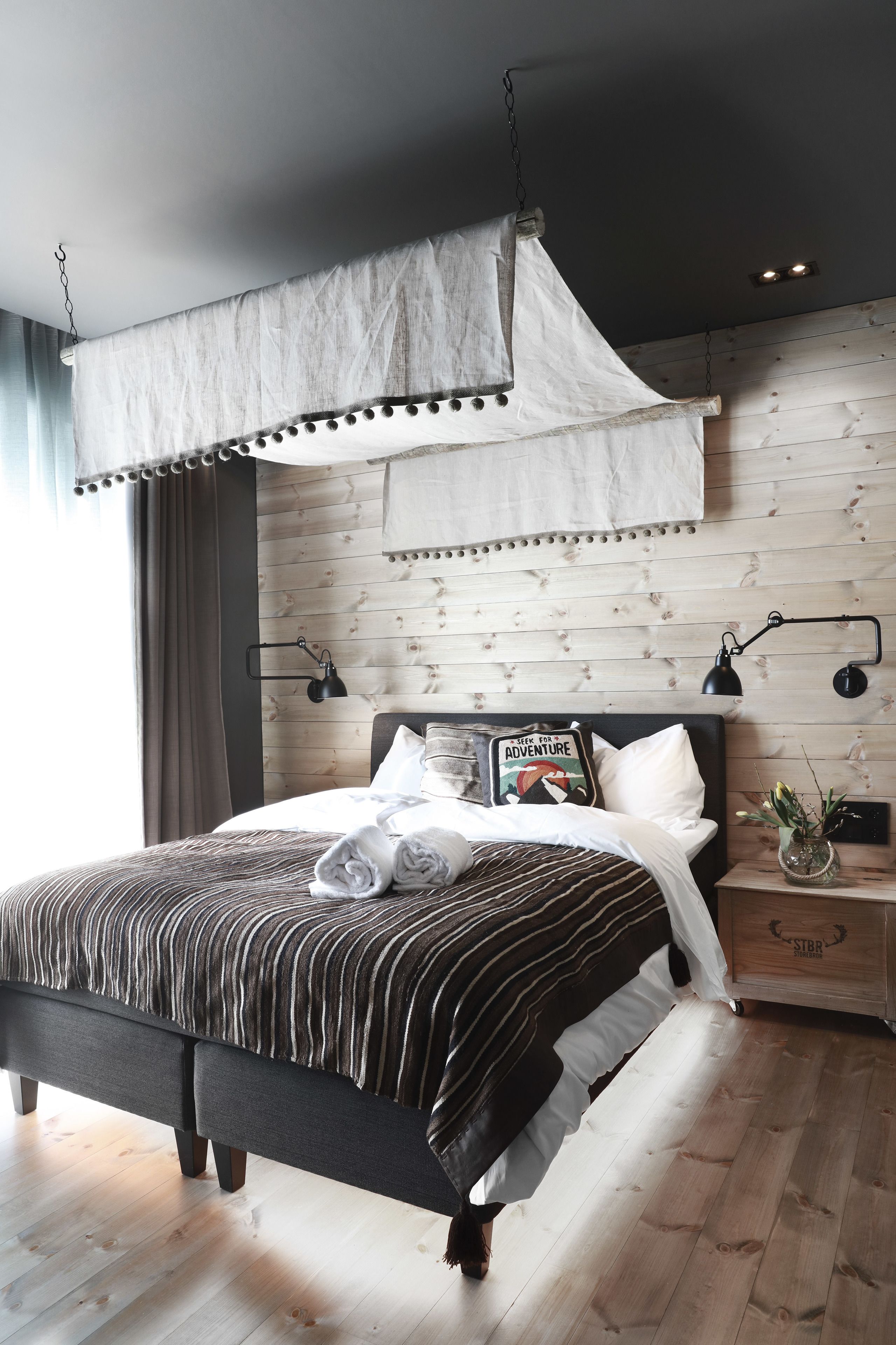 A modern bedroom with a bed, bedside lamps, a nightstand, and a wooden headboard.