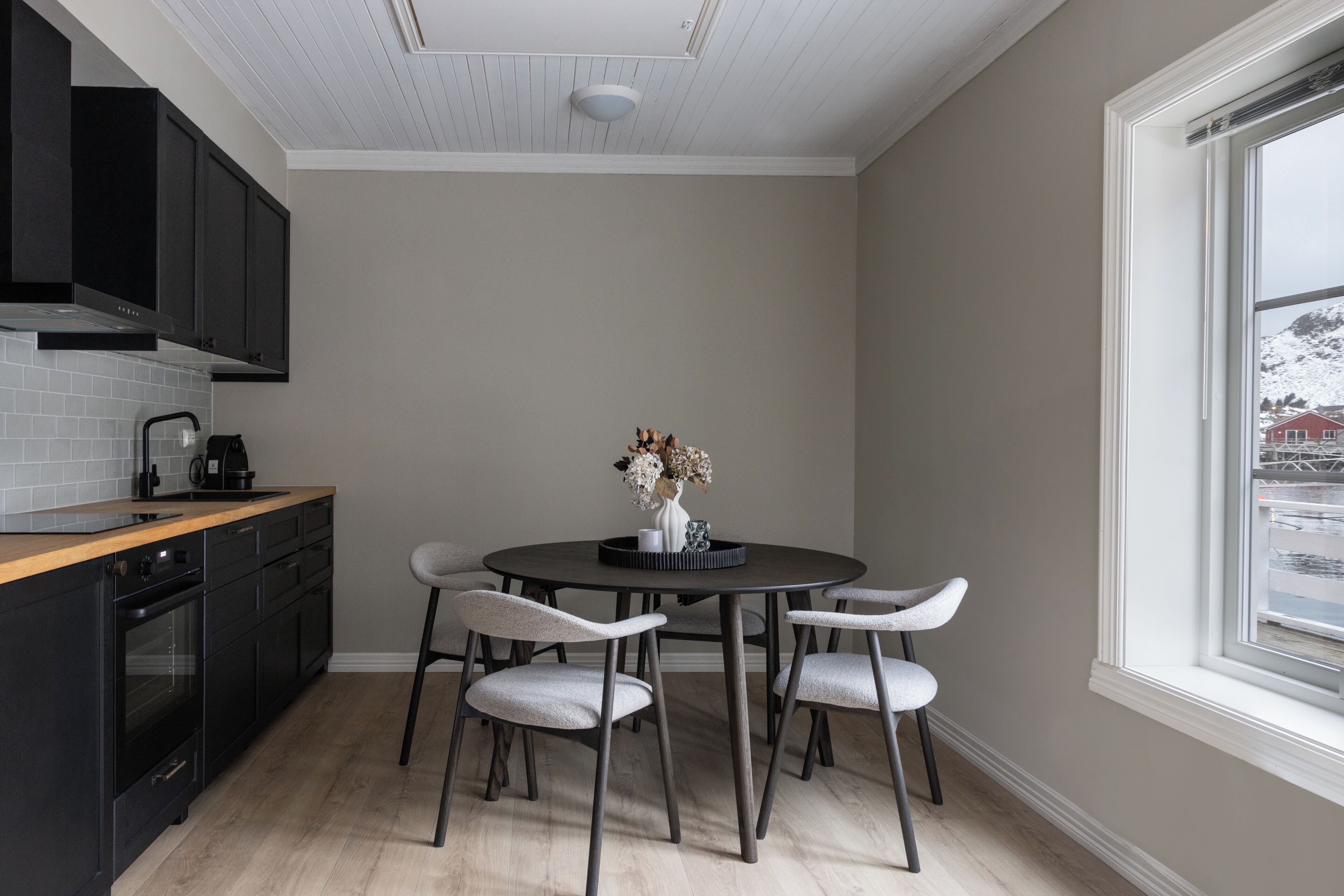 A kitchen with a round dining table, four chairs, a coffee maker, and a window with a view of a snowy landscape.