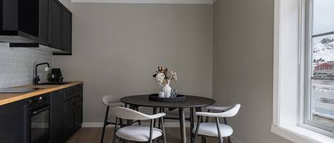 A kitchen with a round dining table, four chairs, a coffee maker, and a window with a view of a snowy landscape.