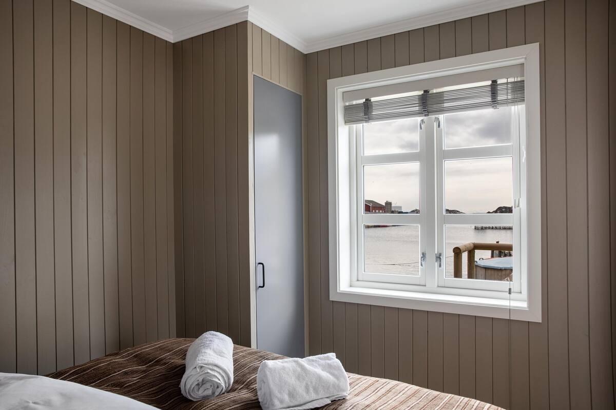 Une chambre avec un lit, une fenêtre donnant sur la mer et une porte.