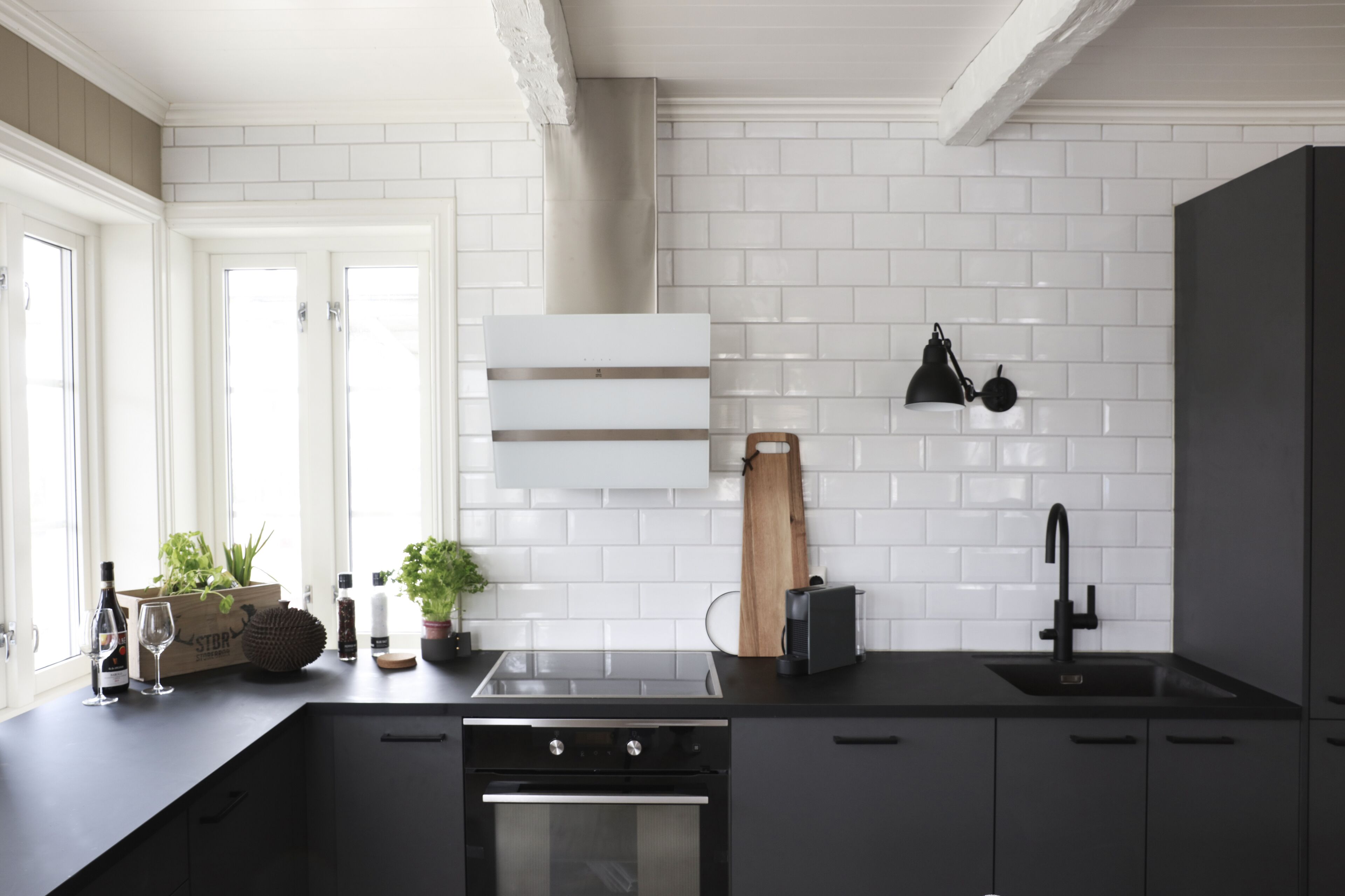 A modern kitchen with white subway tiles, a black countertop, a stainless steel range hood, and a black faucet.
