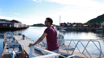 A man standing on a dock with boats, a wooden pier, and buildings in the background.