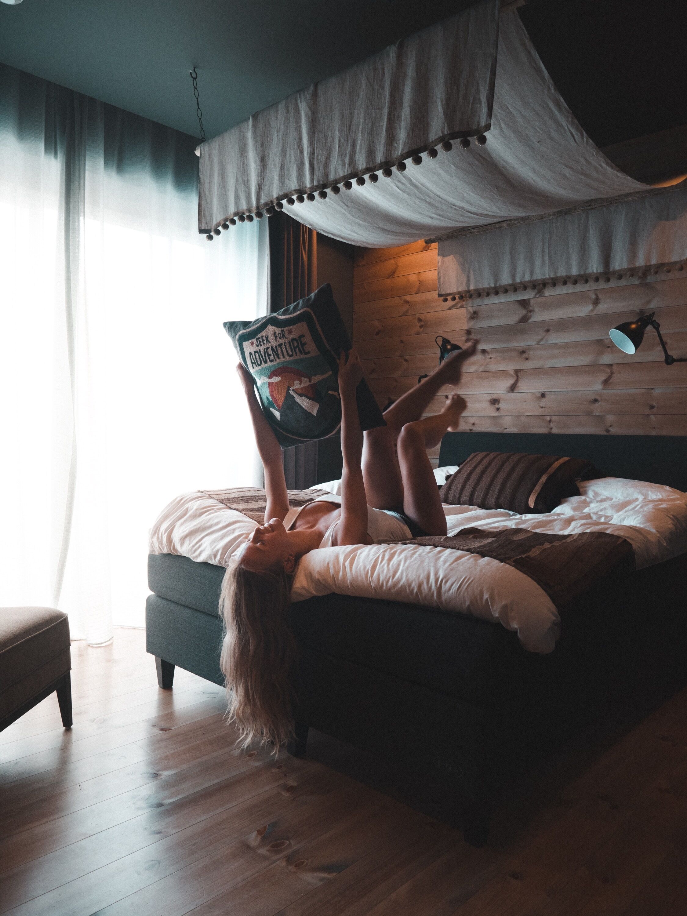 A person lying on a bed with a book titled "Seek for Adventure" and a canopy overhead.