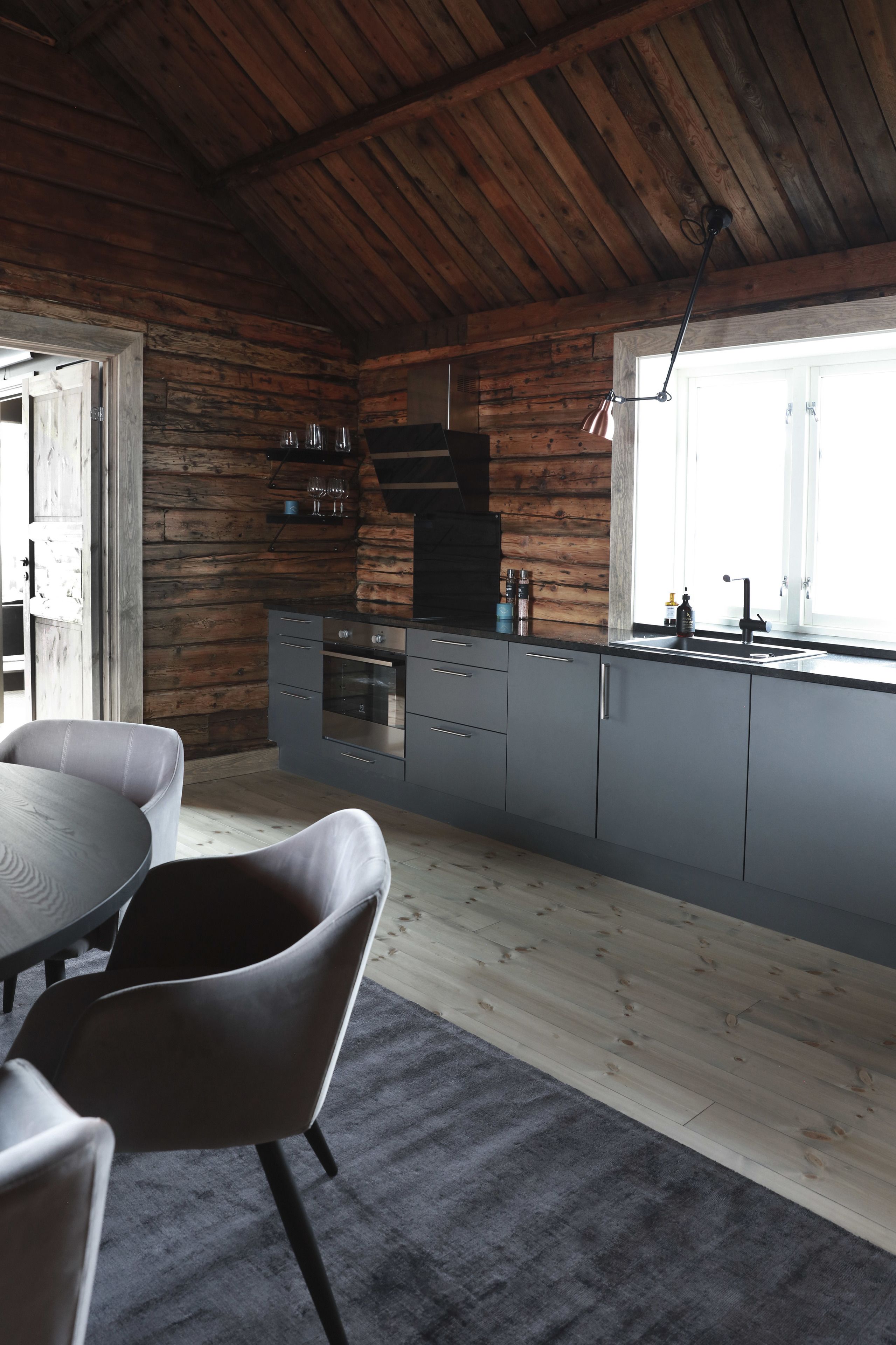 A modern kitchen with wooden walls, grey cabinets, and a large window.