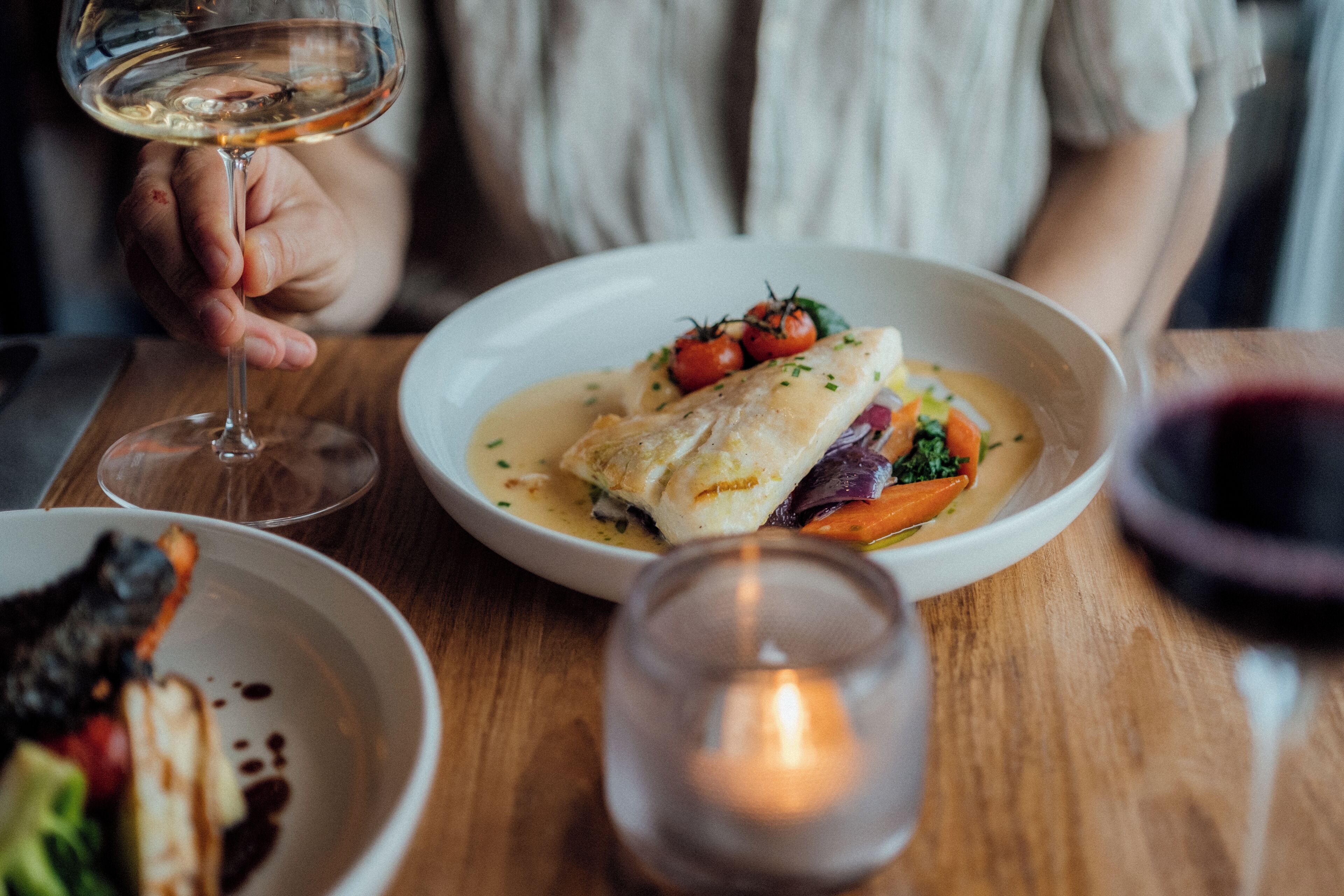 A dining table with a plate of food, a glass of wine, and a candle.