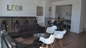 A modern living room with a black sofa, white chairs, a coffee table, and a dining area with a wooden table and chairs.