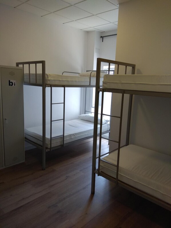A dormitory room with bunk beds, a small cabinet, and a window. - Check in Leon - Hostel (León)