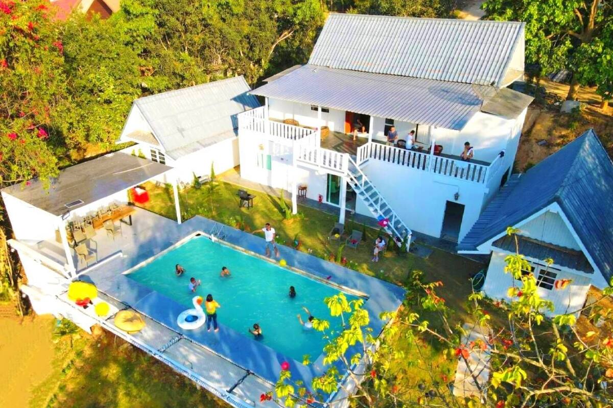 A large swimming pool with a slide, surrounded by a white building with a balcony and a covered patio area.