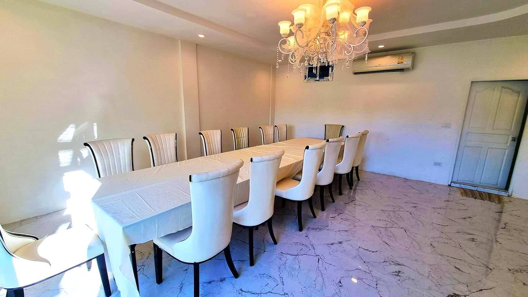 A dining room with a long table and chairs, a chandelier, and an air conditioning unit on the wall.