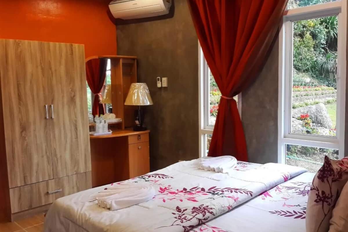A bedroom with a bed, a wooden wardrobe, a desk with a lamp, and a window with curtains.