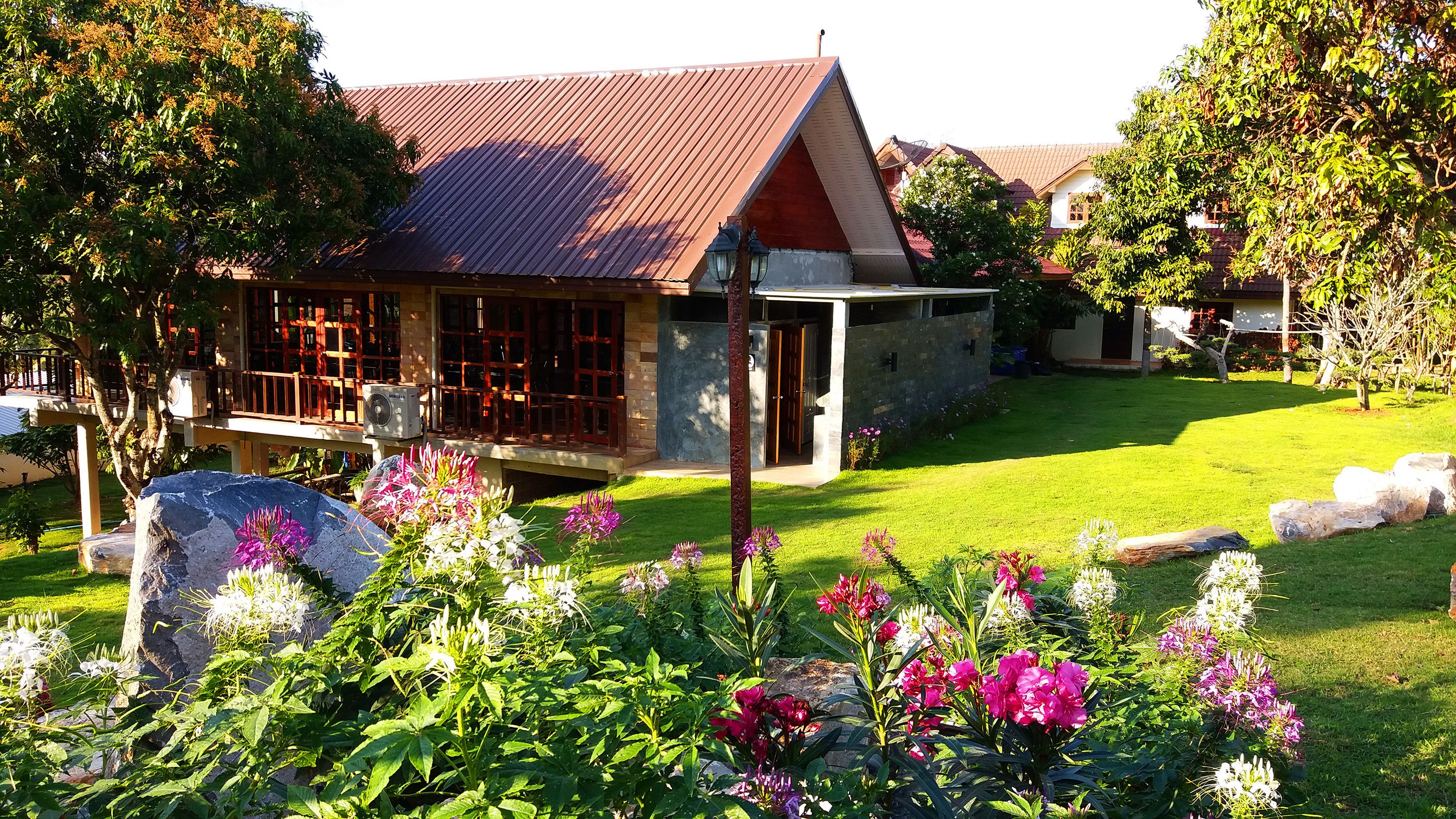 Ein Haus mit rotem Dach, einer Steinfassade und einem gepflegten Rasen mit bunten Blumen.