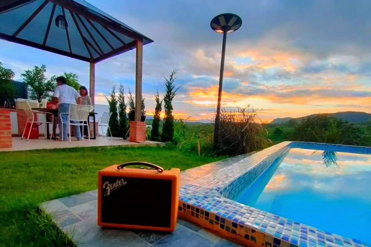 A pool with a tiled edge, a guitar amplifier, a gazebo, and a dining area with people.