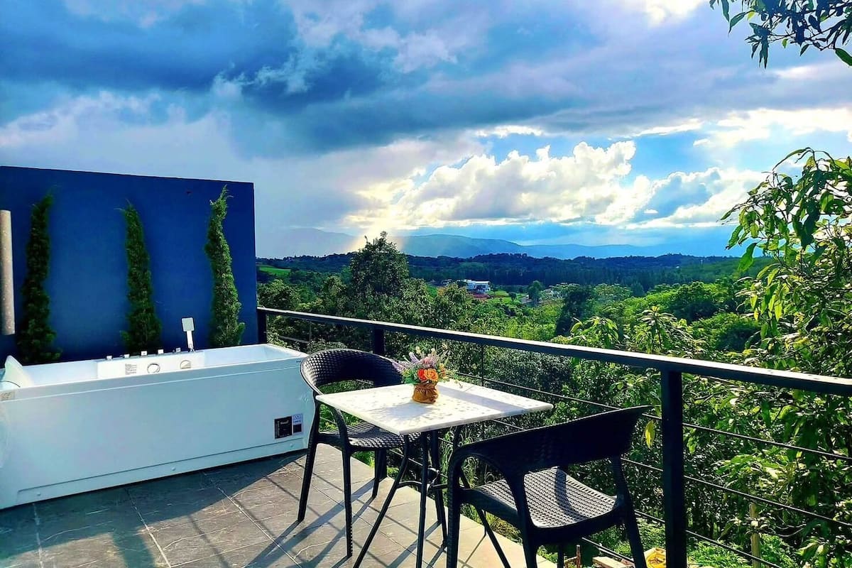 A balcony with a white outdoor seating area, a blue wall, and a view of a green landscape.