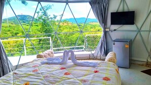 A bedroom with a bed, a TV, and a view of green hills. - Kirirath Resort (Pak Chong)