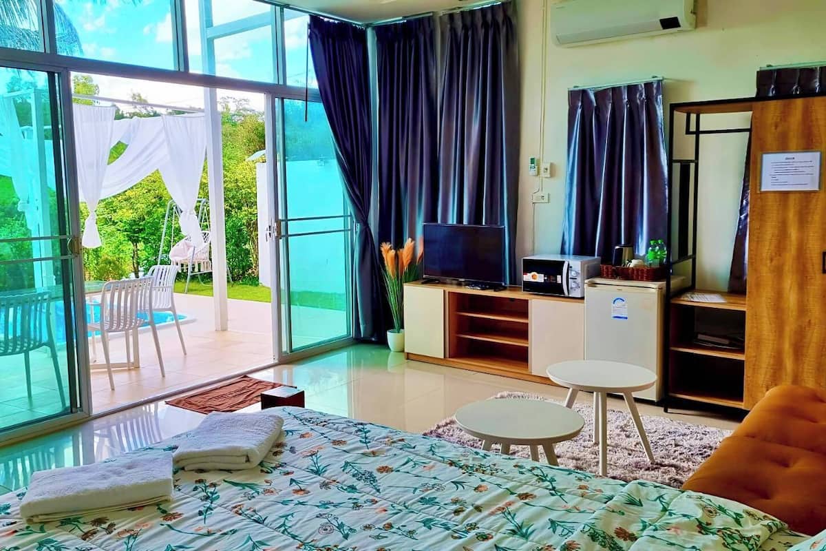 A hotel room with a bed, a TV, a small table, and a sofa. There is a sliding glass door leading to an outdoor area with chairs and a table.
