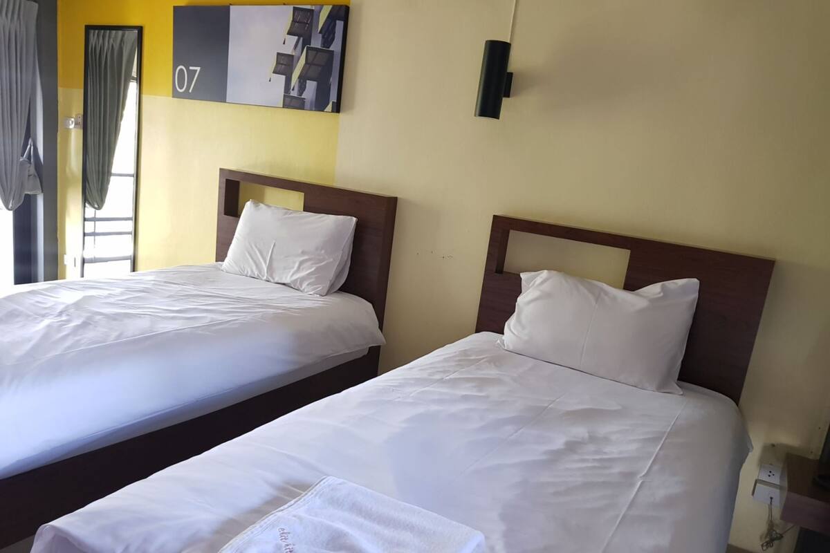A hotel room with two beds, each with white linens and pillows, a wooden headboard, and a painting on the wall.