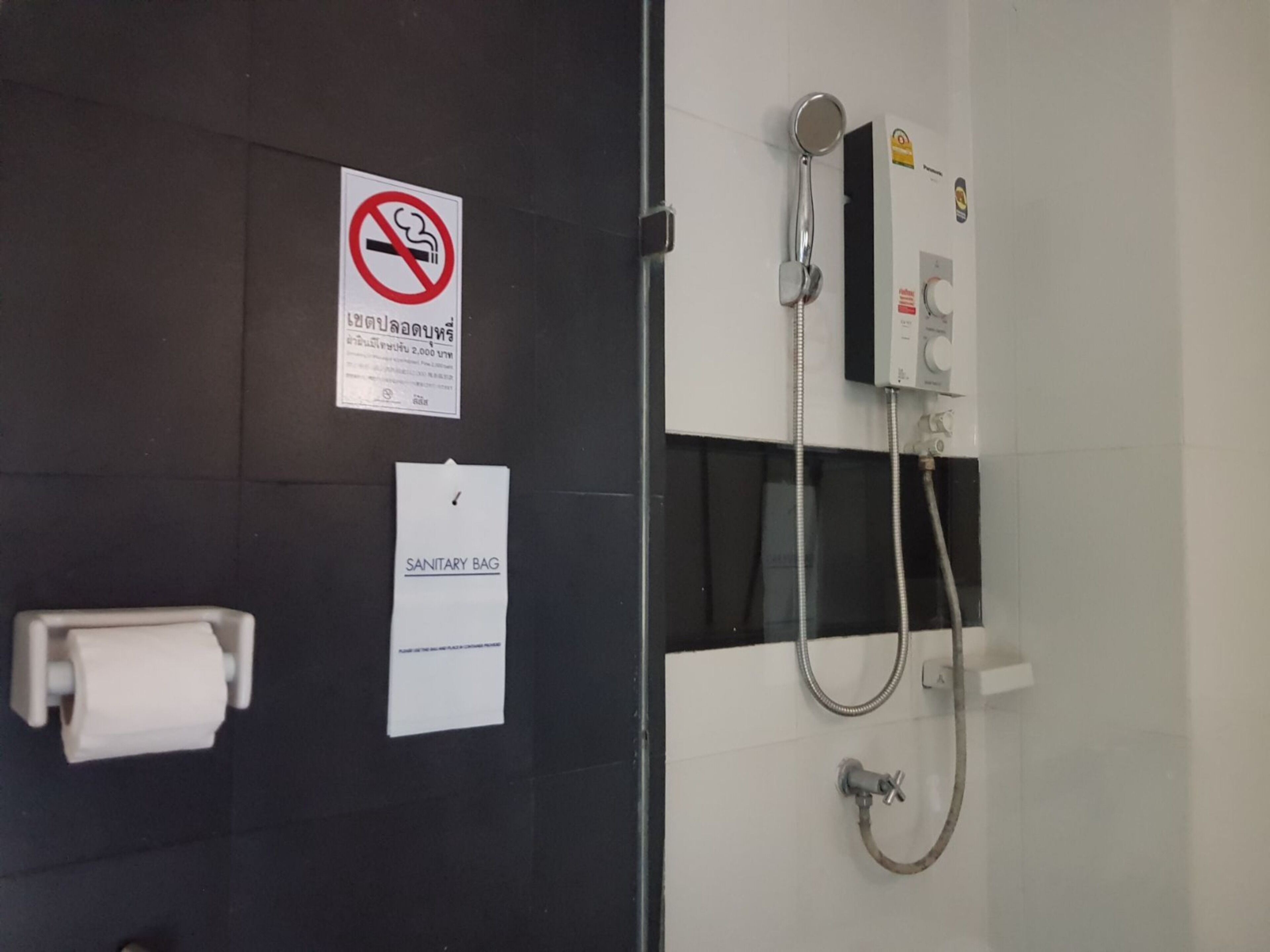 A bathroom with a shower, a toilet, and a no-smoking sign.
