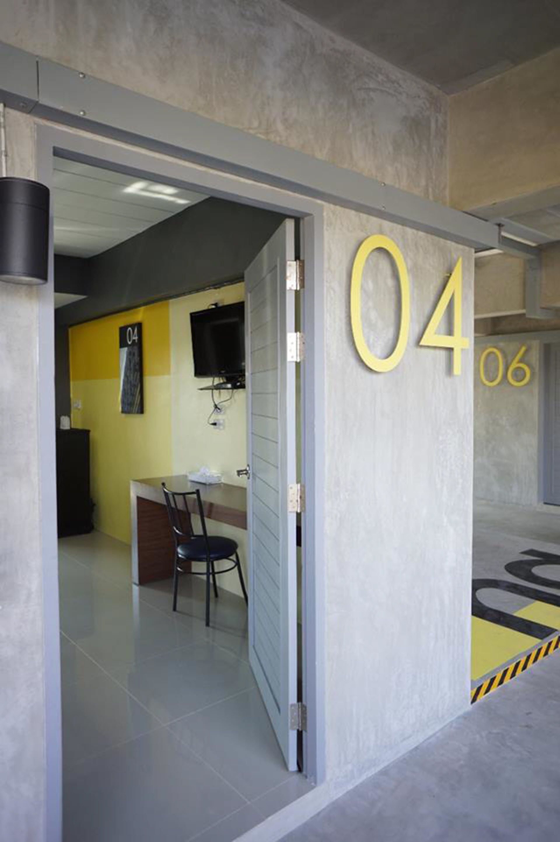 Una habitación de hotel moderna con el número '04' en la pared, un escritorio con una silla y un televisor montado.