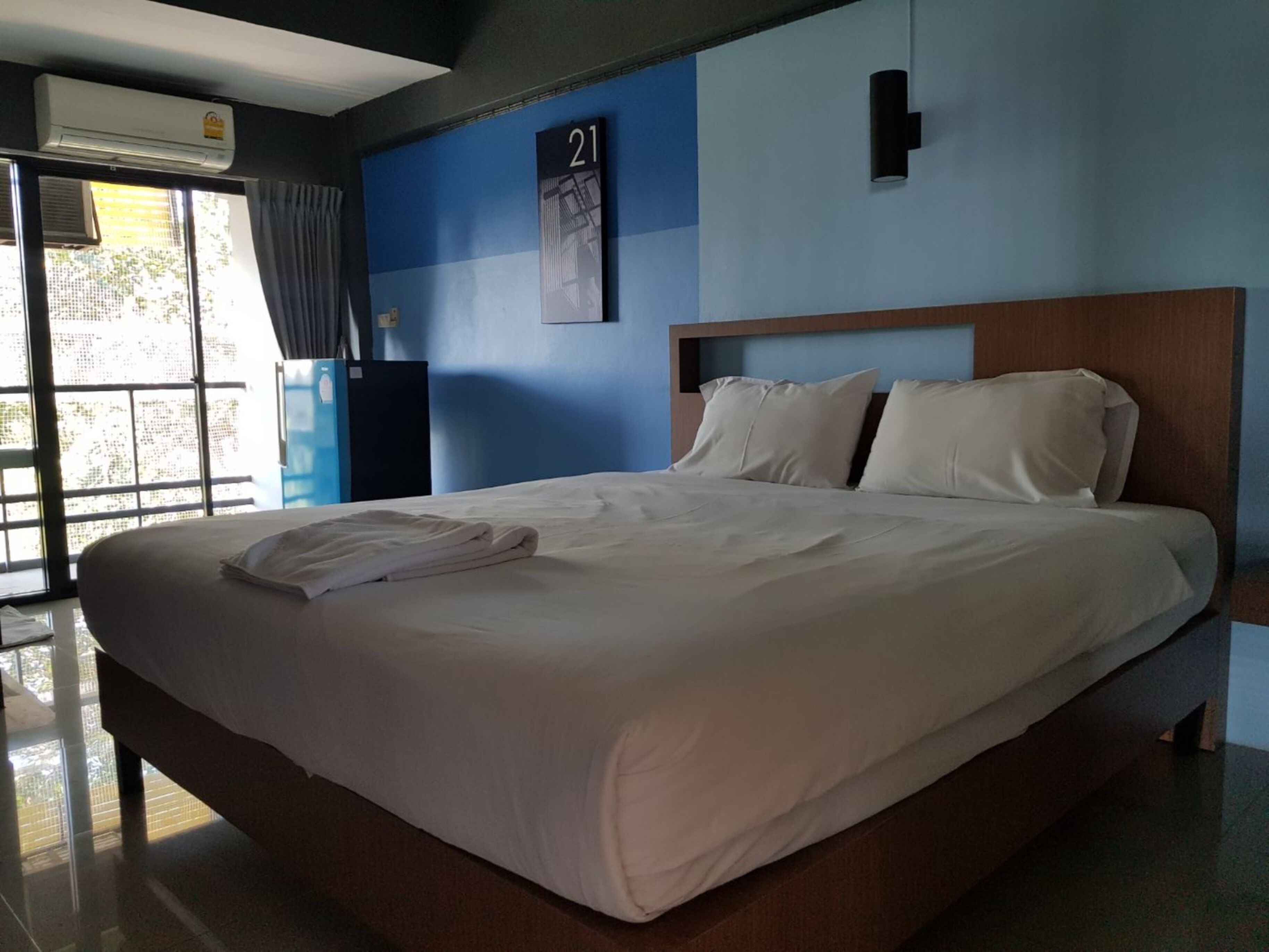 Una cama bien tendida con sábanas blancas en una habitación de hotel con una pared azul decorativa y un cartel con un número.