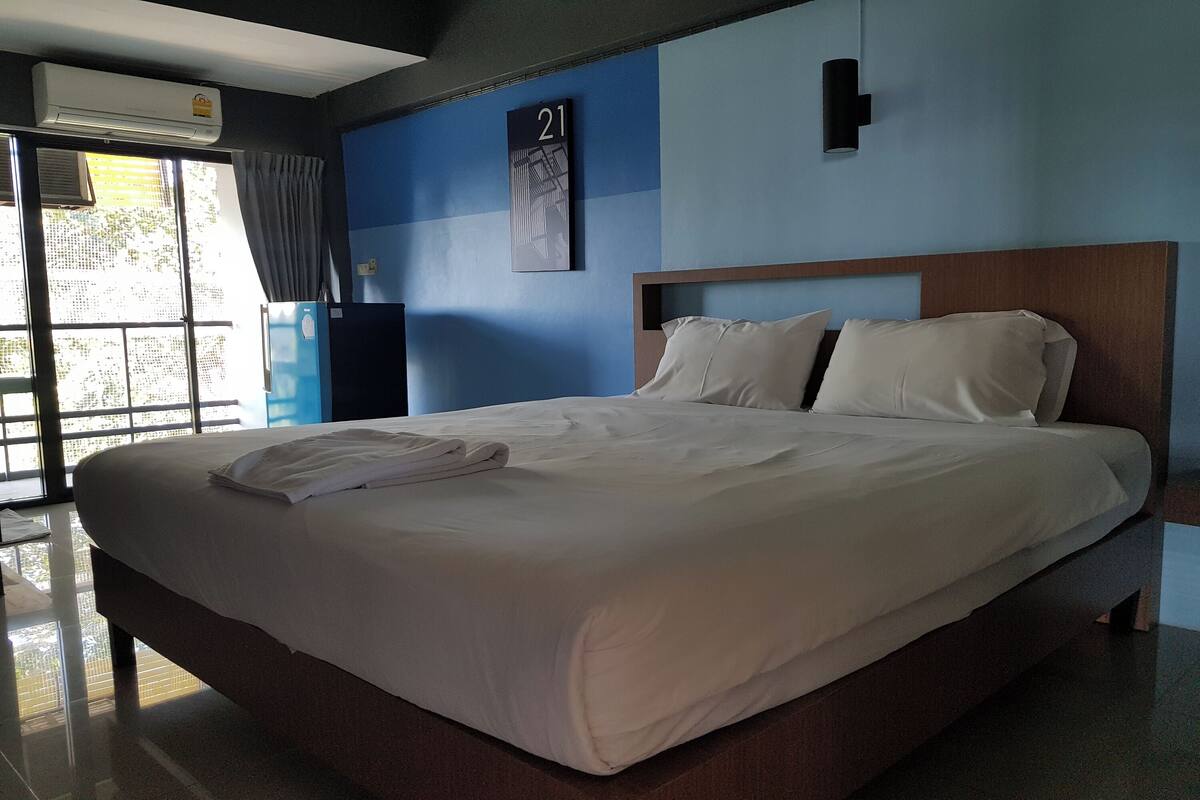A hotel room with a large bed, a wall-mounted air conditioner, a number sign, and a window with curtains.