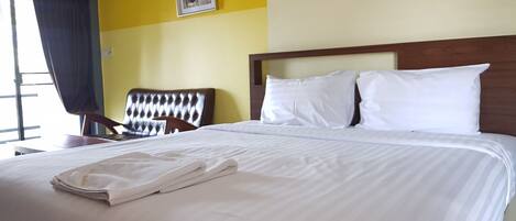 A neatly made bed with white linens and a folded towel, a wooden headboard, a chair, and a wall-mounted picture.