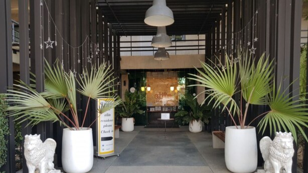 A hotel entrance with a check-in desk, potted plants, and two lion statues. - Elite Residence Phitsanulok (Phitsanulok)