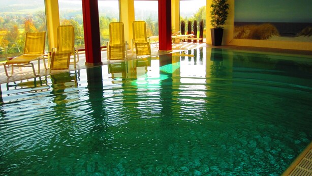 Una piscina interior con agua cristalina, sillas amarillas y grandes ventanales que ofrecen vistas al exterior.