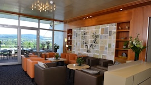 Un área de estar moderna con asientos cómodos, una pared decorada con cuadros enmarcados y vistas al exterior.