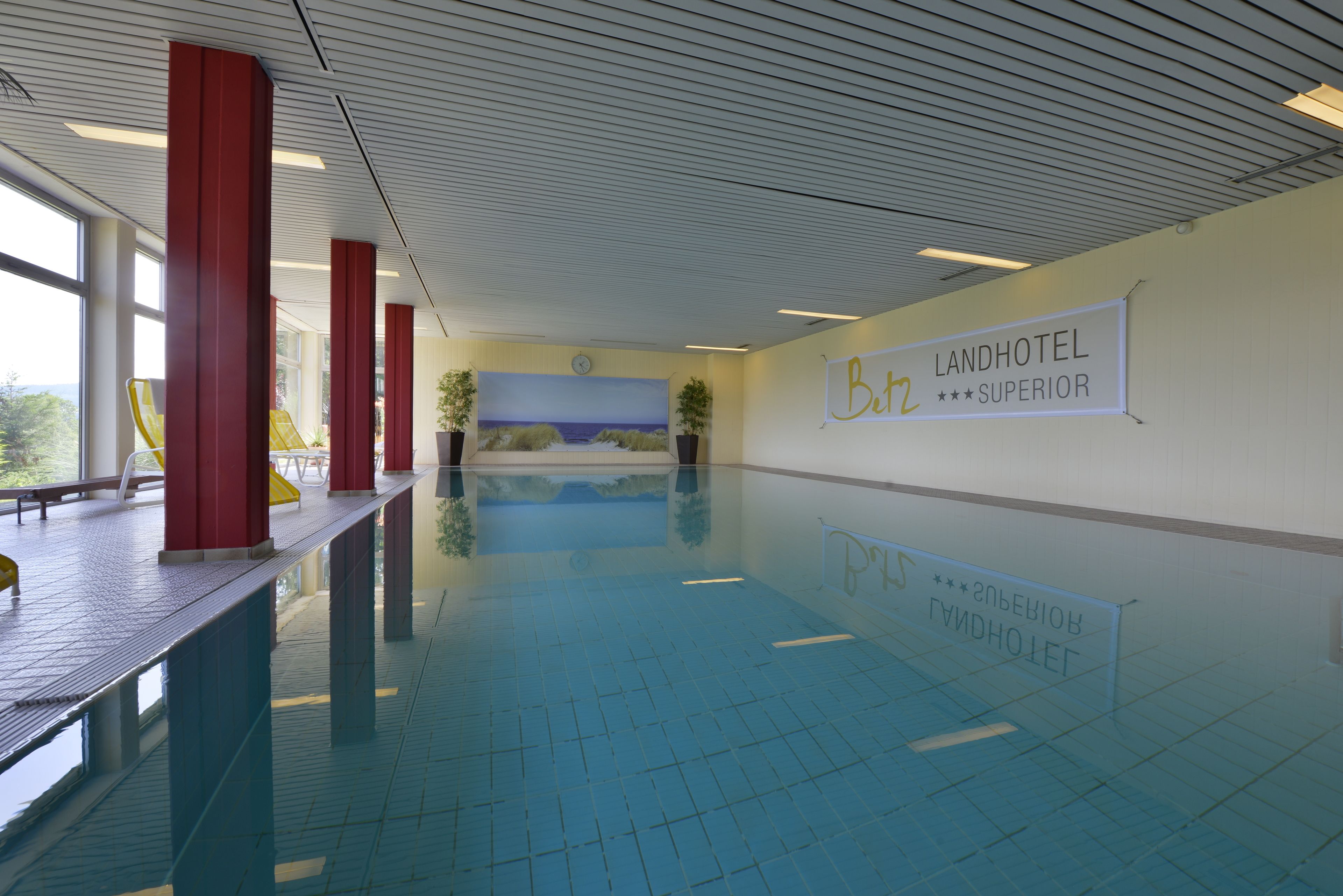 A swimming pool with red pillars, a mural, and a sign for 'Landhotel Betz Superior'.