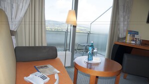 Habitación de hotel con balcón, un sofá, una mesita con lámpara, teléfono y botella de agua.