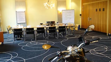 Une salle de conférence avec une longue table, des chaises, un tableau blanc et une moto au premier plan.