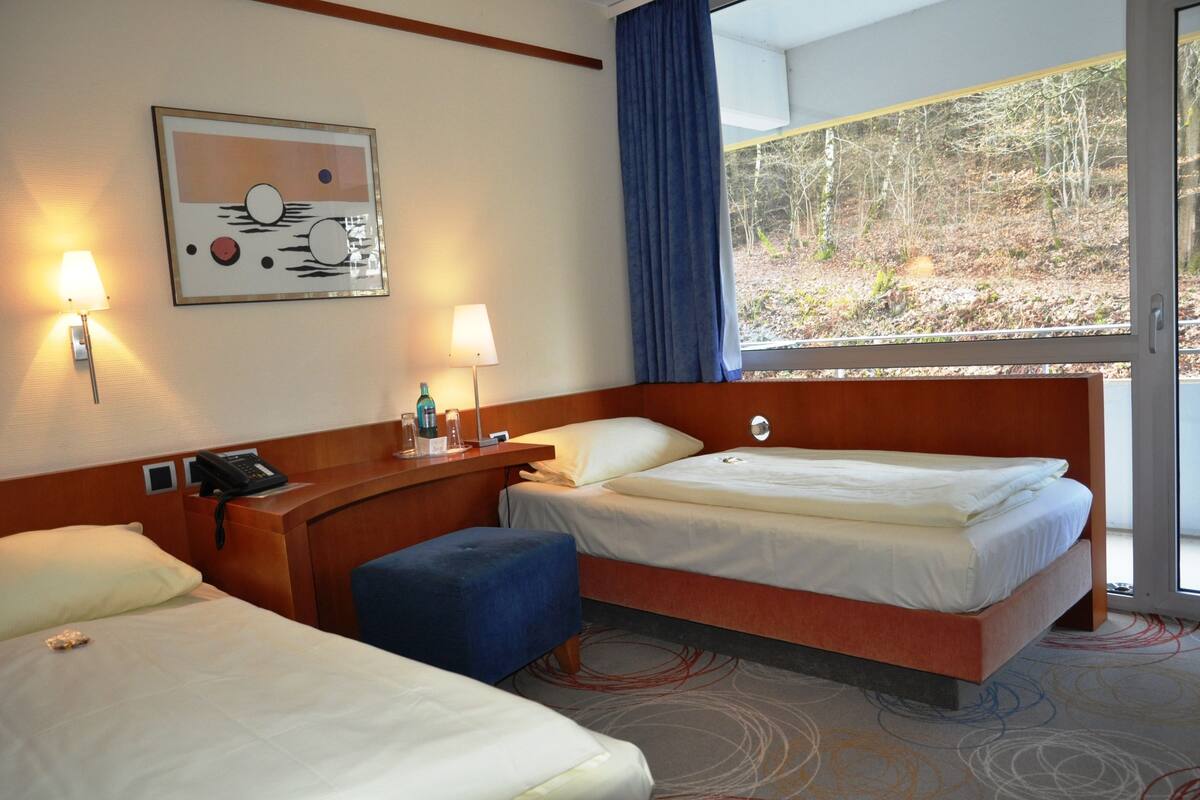 Habitación de hotel con dos camas, un escritorio, un teléfono y una ventana que da a árboles.