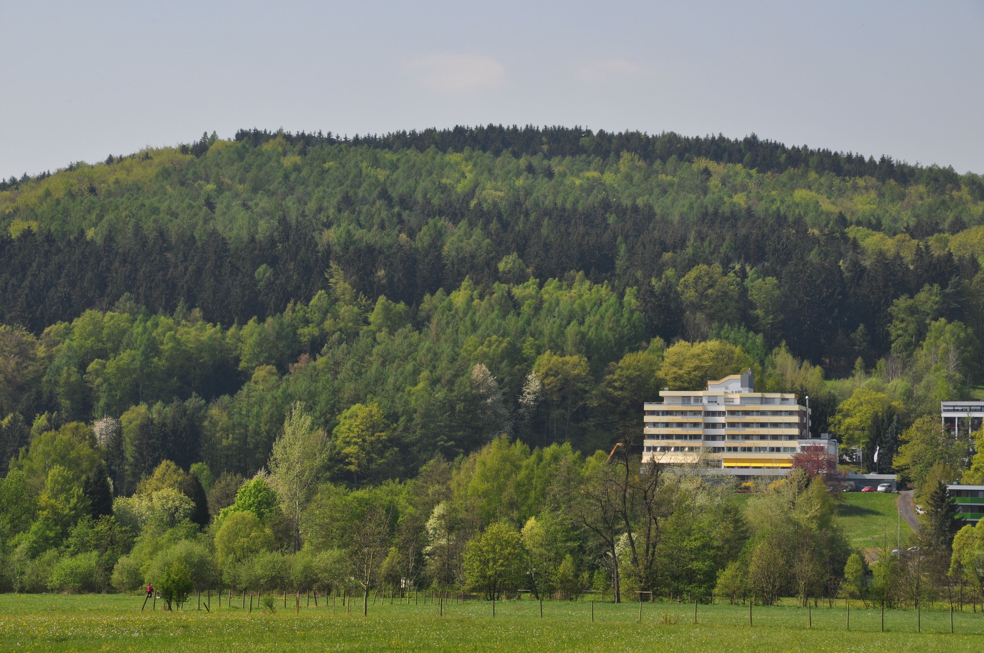 Ein mehrstöckiges Gebäude, umgeben von einer grünen Landschaft mit Bäumen und einer Hügelkulisse.