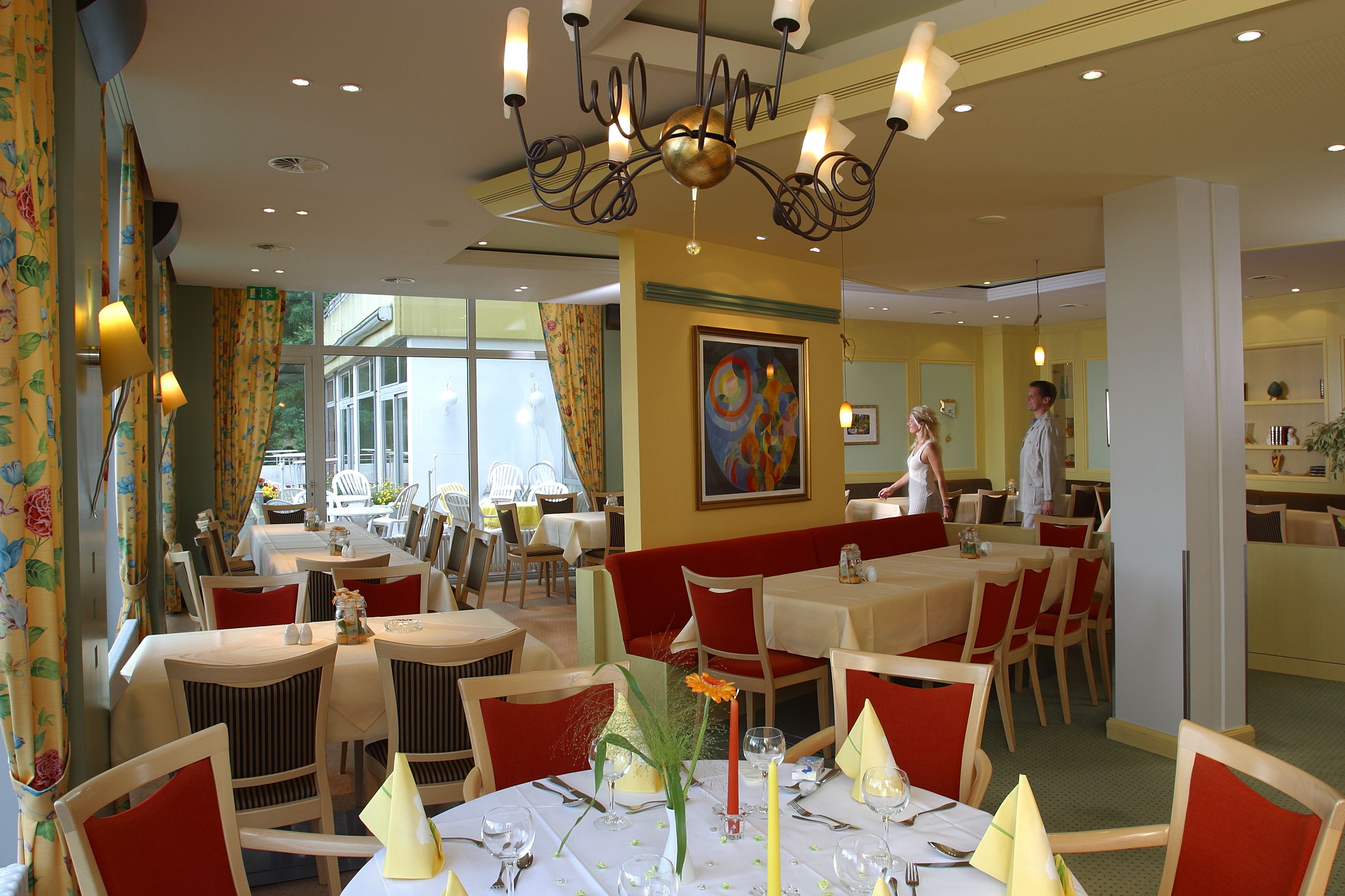 A restaurant with round tables, red cushioned booths, and a chandelier.