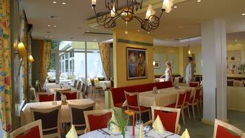 A restaurant with round tables, red cushioned booths, and a chandelier.