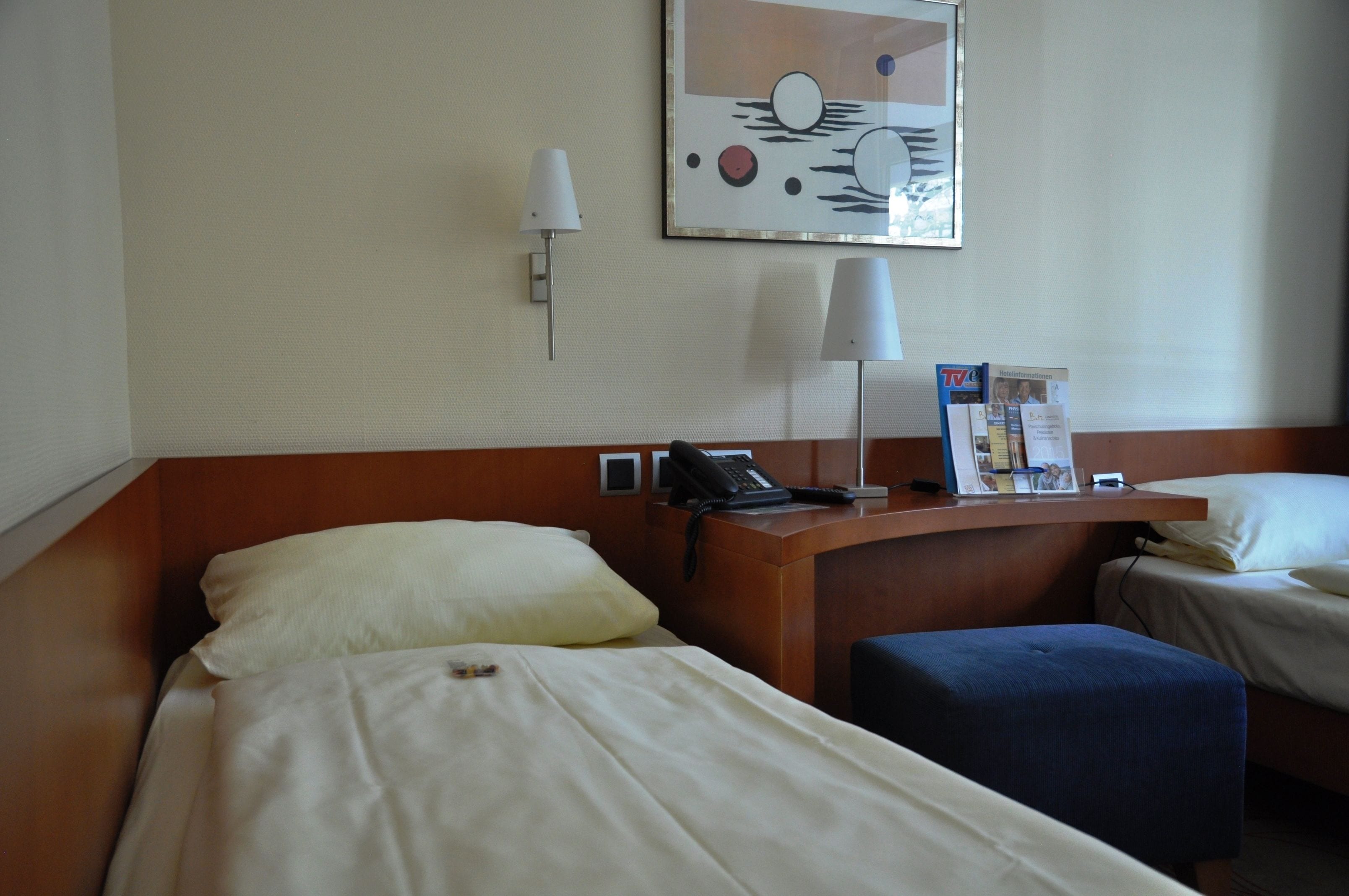 Une chambre d’hôtel avec deux lits, un bureau doté d’un téléphone, une lampe et une œuvre d’art accrochée au mur.