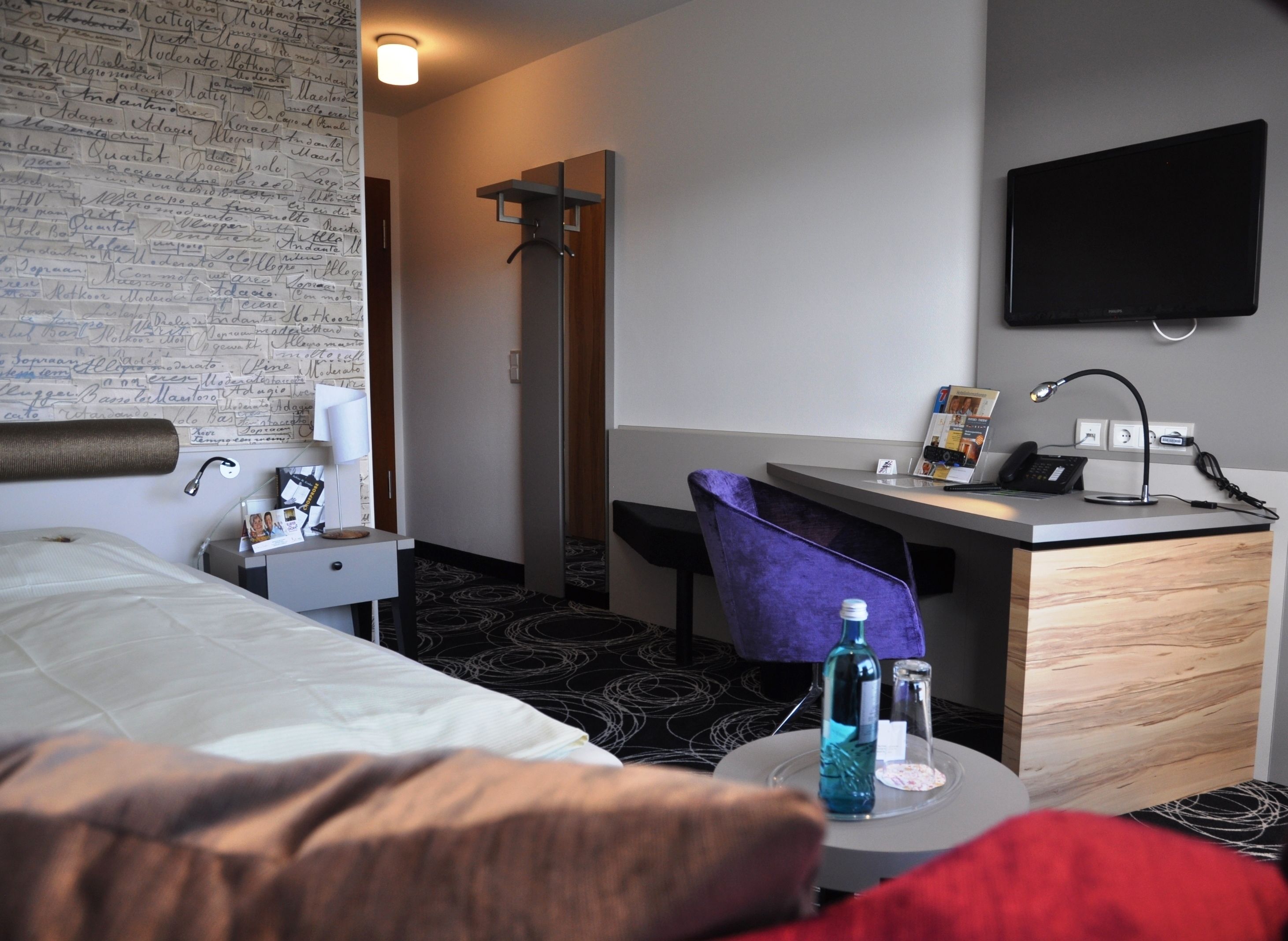 A hotel room with a bed, a desk, a chair, a TV, and a wall with handwritten notes.