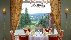 Un comedor con una mesa dispuesta para cuatro, sillas rojas y vistas a un paisaje verde a través del ventanal.