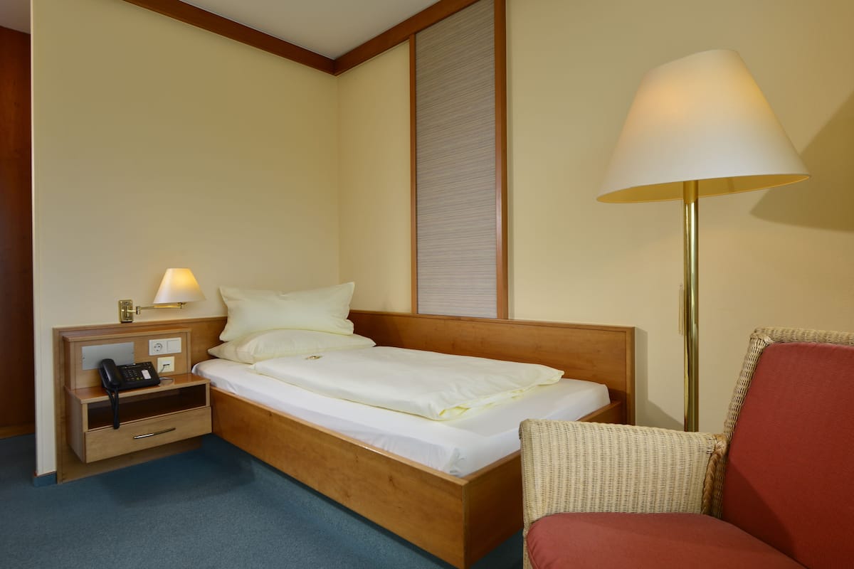 Una habitación de hotel con una cama de madera, una mesita de noche con lámpara, una silla y un teléfono.