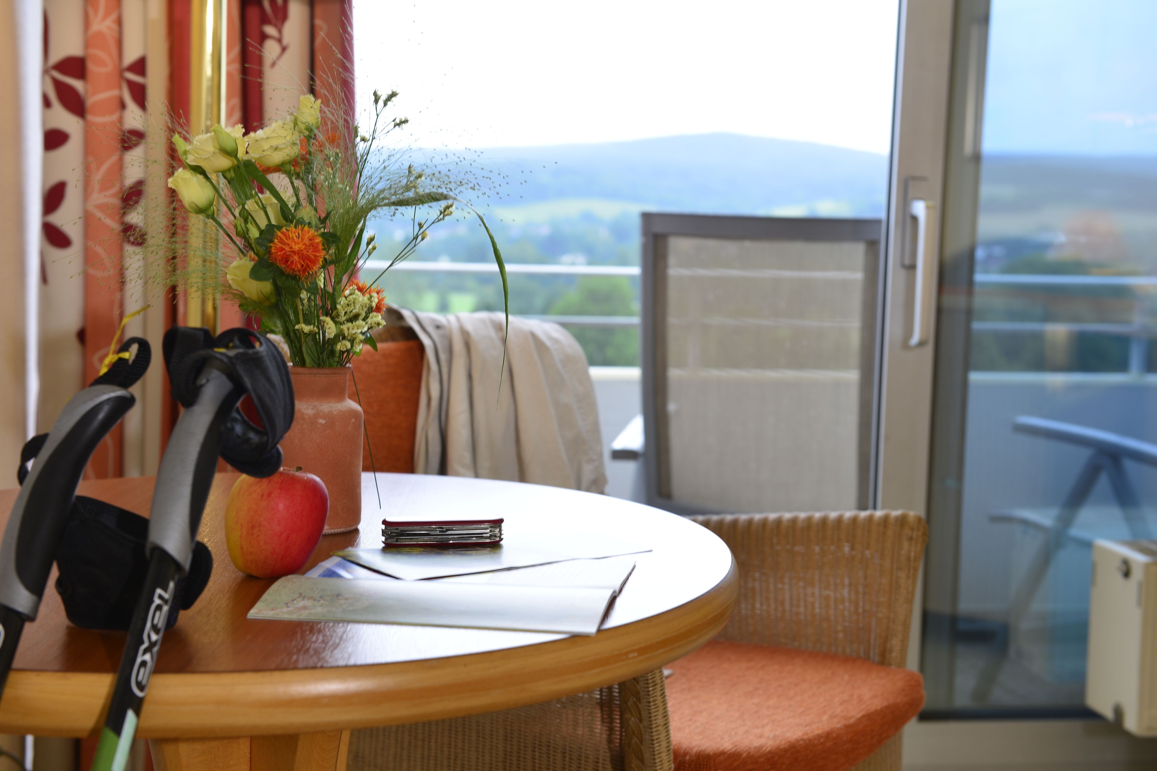 Una habitación con una mesa, una silla, dos muletas, un jarrón con flores y vistas al exterior.
