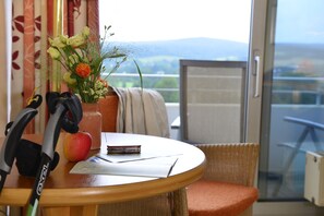 A room with a table, a chair, a pair of crutches, a vase with flowers, and a view of the outdoors. - Trip Inn Landhotel Bad Soden-Salmünster (Bad Soden-Salmuenster)