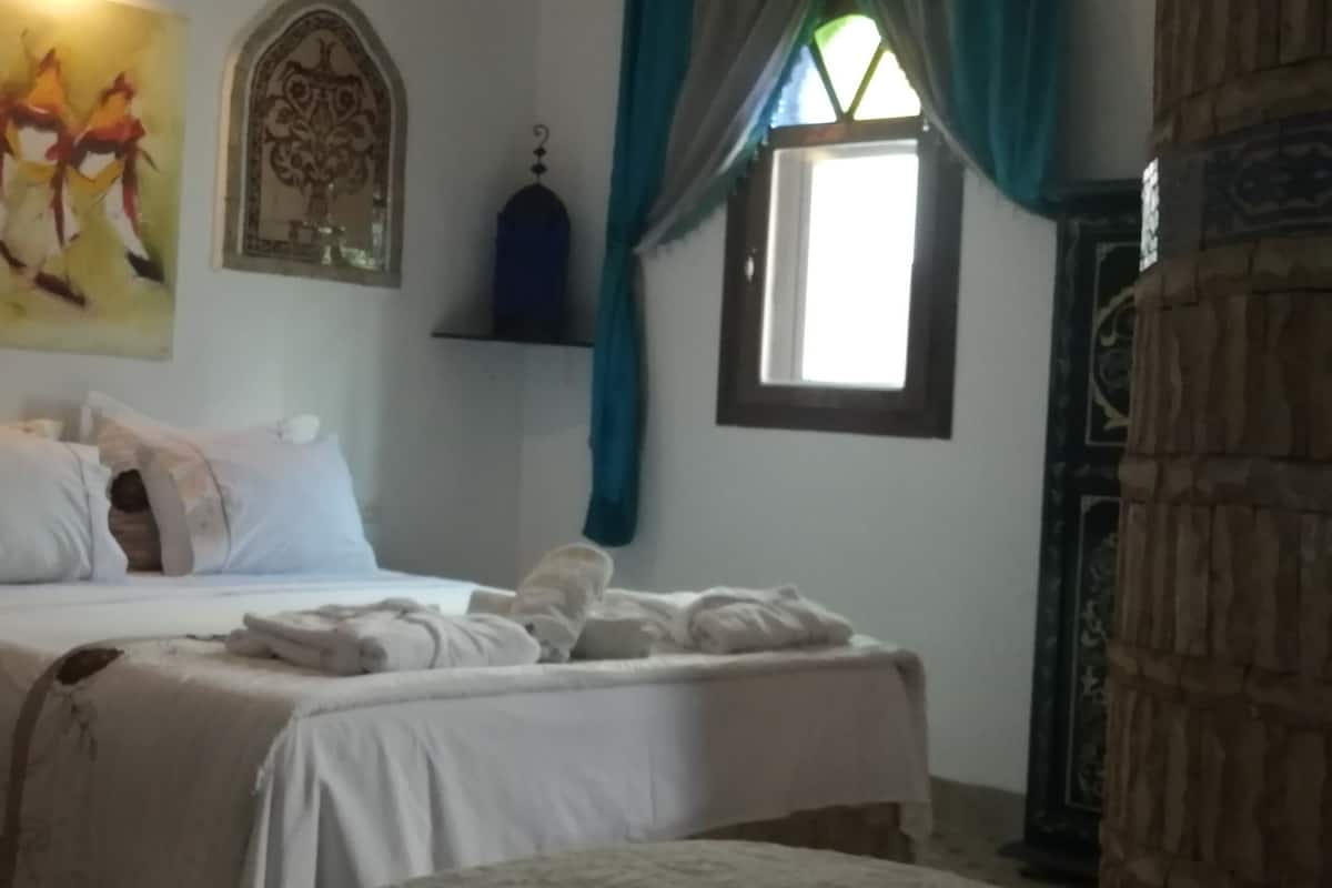 Una cama bien tendida con sábanas blancas, una silla y un adorno en la pared.